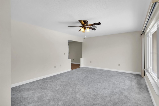 spare room featuring a textured ceiling, carpet, a ceiling fan, and baseboards