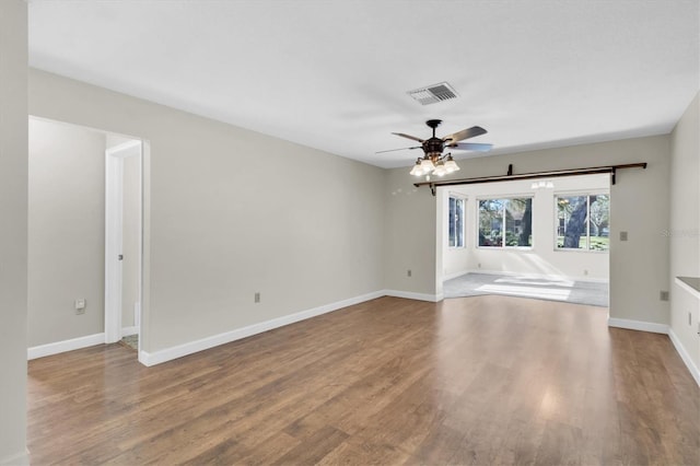 unfurnished room featuring baseboards, wood finished floors, visible vents, and a ceiling fan