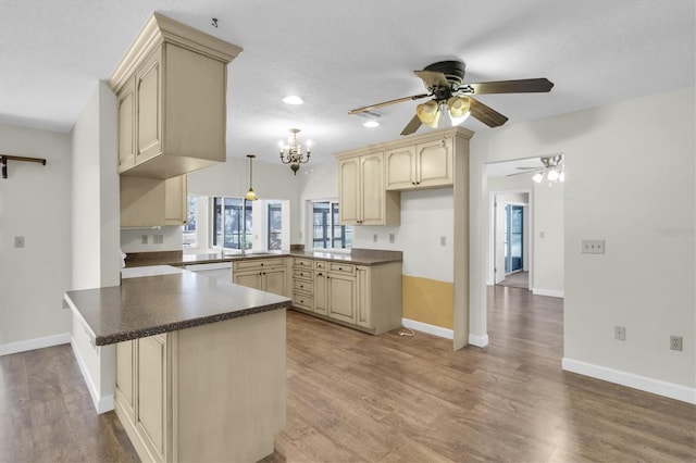 kitchen with dark countertops, cream cabinets, wood finished floors, a peninsula, and baseboards