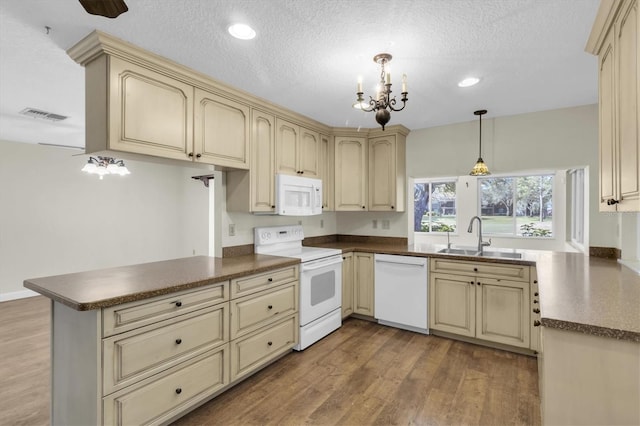 kitchen with cream cabinetry, dark countertops, a sink, white appliances, and a peninsula