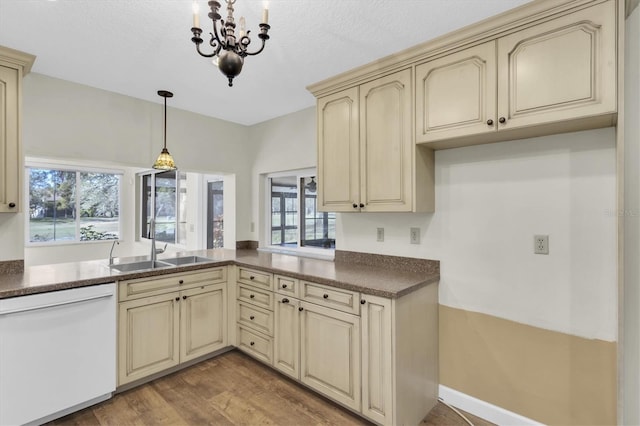 kitchen featuring cream cabinets, wood finished floors, a sink, dishwasher, and dark countertops