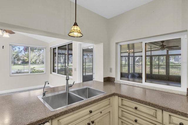 kitchen with a ceiling fan, dark countertops, cream cabinets, pendant lighting, and a sink