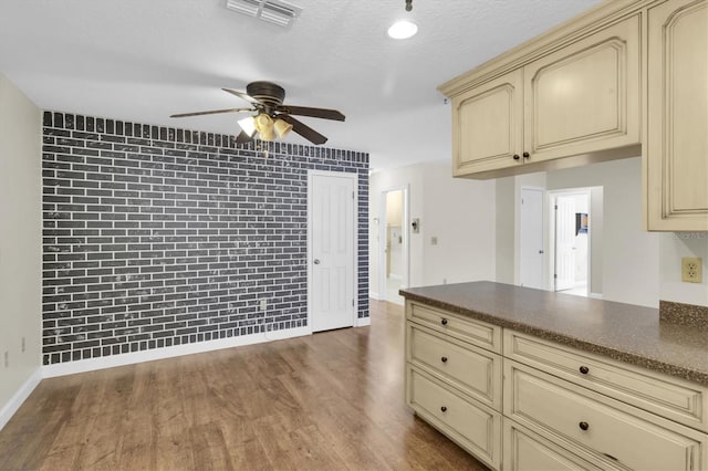 kitchen featuring dark wood-style floors, cream cabinets, dark countertops, and visible vents