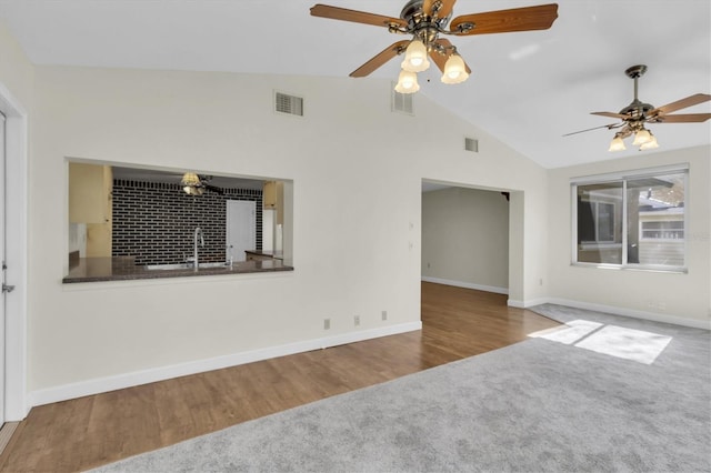 unfurnished living room with baseboards, visible vents, vaulted ceiling, and wood finished floors