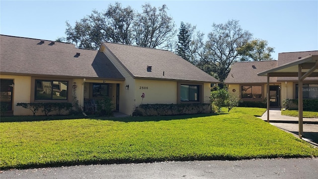 view of front facade with roof with shingles, a front yard, and stucco siding