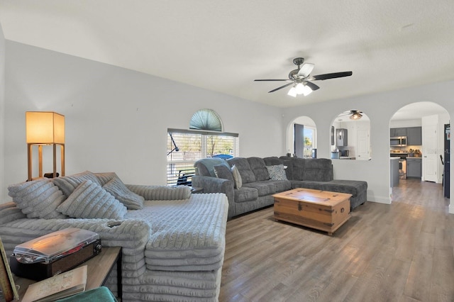 living area featuring a ceiling fan, arched walkways, baseboards, and wood finished floors