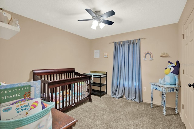 carpeted bedroom featuring a nursery area and ceiling fan