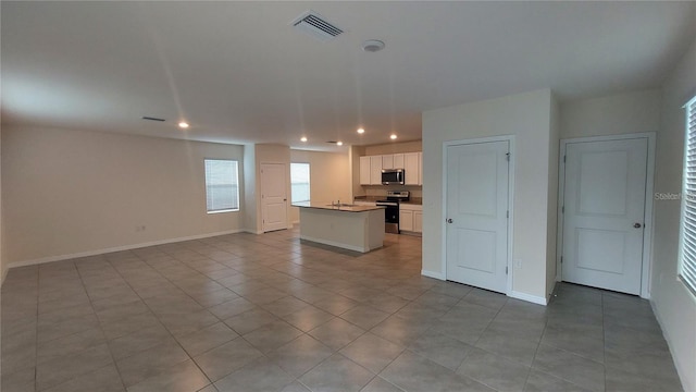 kitchen with a center island with sink, visible vents, white cabinets, open floor plan, and stainless steel appliances