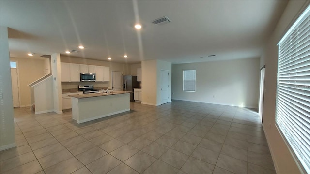 kitchen featuring stainless steel appliances, open floor plan, visible vents, and an island with sink