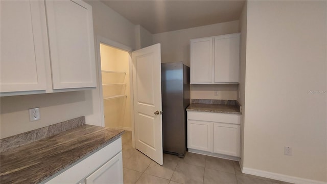 kitchen with light tile patterned floors, white cabinetry, and baseboards