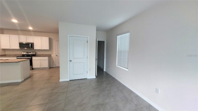 kitchen with stainless steel appliances, white cabinets, a sink, light tile patterned flooring, and baseboards