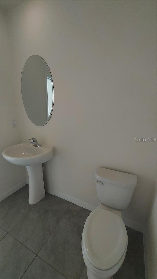 half bath with tile patterned flooring, toilet, and baseboards