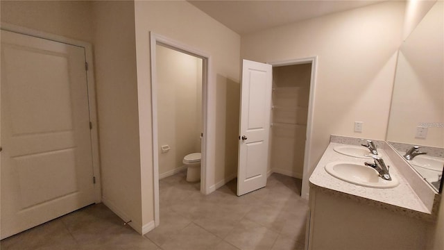 bathroom featuring toilet, double vanity, baseboards, and a sink