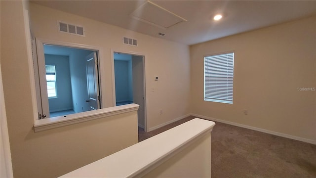 corridor featuring baseboards, dark colored carpet, visible vents, and attic access