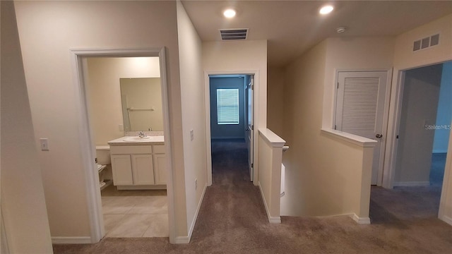 hallway featuring visible vents, light colored carpet, a sink, and an upstairs landing