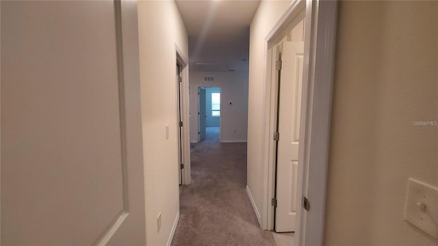 corridor with light colored carpet, visible vents, and baseboards