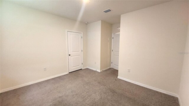 spare room with dark carpet, visible vents, and baseboards