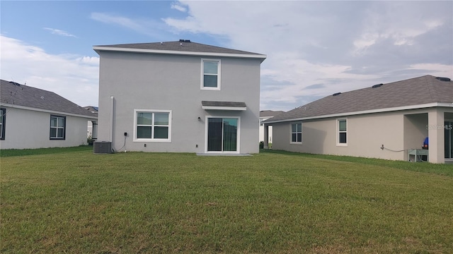 rear view of property with central air condition unit, stucco siding, and a yard