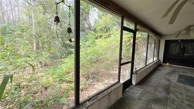 unfurnished sunroom featuring ceiling fan and a wooded view