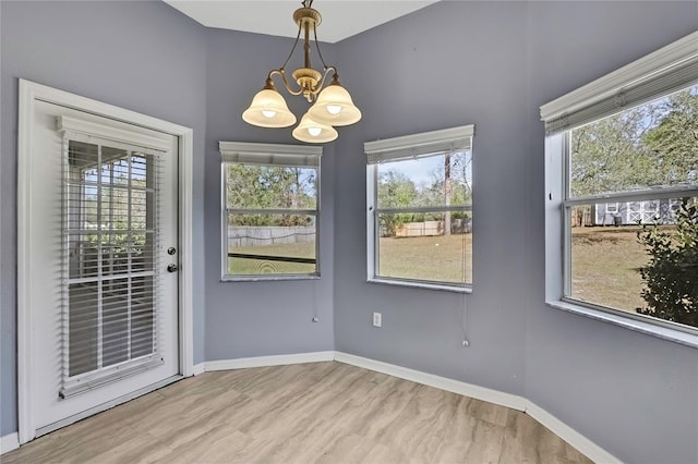 unfurnished dining area featuring baseboards, a chandelier, and wood finished floors