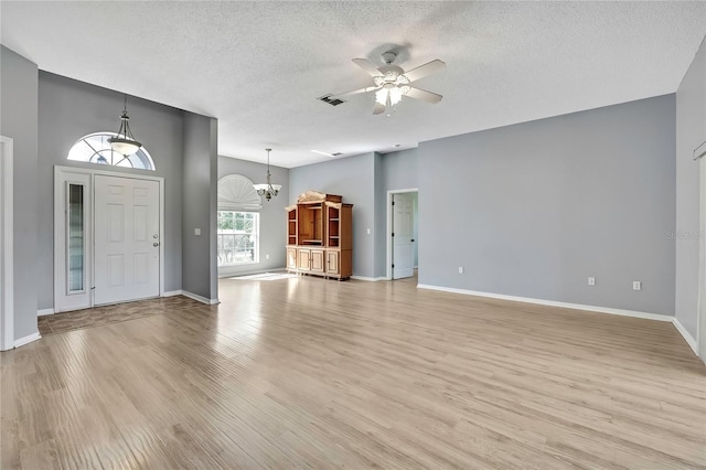 unfurnished living room with ceiling fan with notable chandelier, a textured ceiling, light wood-style flooring, and baseboards