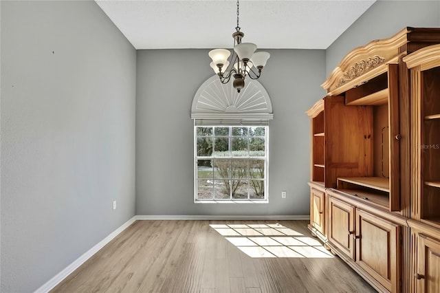 unfurnished dining area featuring a chandelier, light wood-type flooring, and baseboards