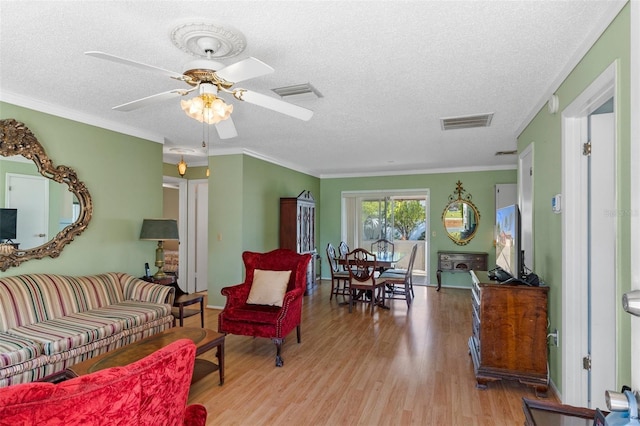 living area featuring light wood-type flooring, visible vents, a textured ceiling, and crown molding