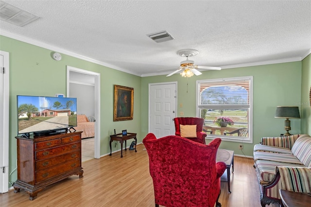 living room featuring light wood finished floors, visible vents, a textured ceiling, and ornamental molding