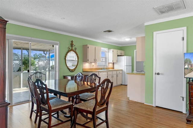 dining space with light wood-type flooring, visible vents, a textured ceiling, and ornamental molding