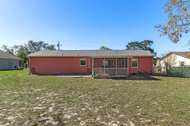 rear view of house with a yard, a sunroom, stucco siding, and fence