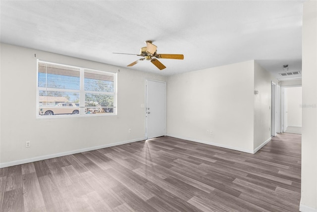 empty room featuring a ceiling fan, visible vents, baseboards, and wood finished floors