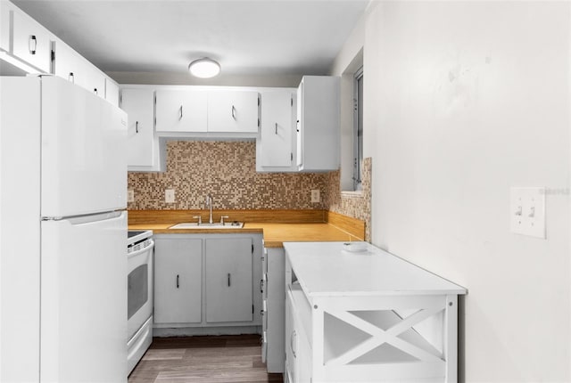 kitchen featuring white appliances, tasteful backsplash, wood finished floors, light countertops, and a sink