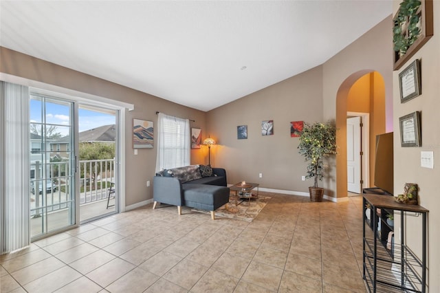 sitting room featuring vaulted ceiling, light tile patterned floors, baseboards, and arched walkways