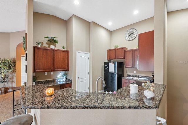 kitchen with a breakfast bar, a peninsula, freestanding refrigerator, a towering ceiling, and arched walkways