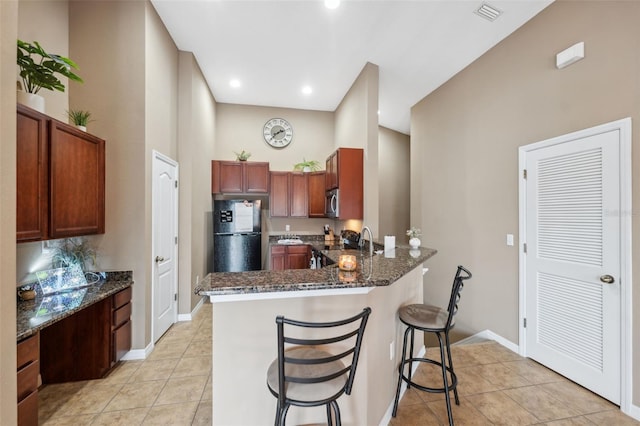 kitchen featuring light tile patterned floors, dark stone countertops, a peninsula, and stainless steel appliances