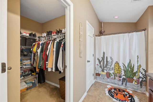 interior space with a walk in closet, tile patterned floors, a shower with curtain, and baseboards