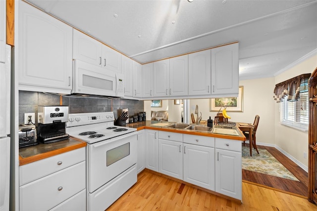 kitchen with white cabinets, white appliances, a peninsula, and a sink