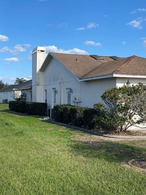 view of front of house with a shingled roof, a chimney, a front lawn, and stucco siding