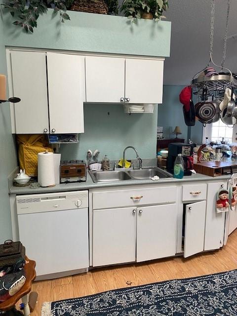 kitchen with light countertops, white cabinets, white dishwasher, and a sink