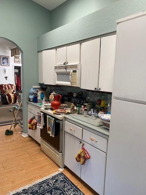 kitchen with light wood-type flooring, white appliances, arched walkways, and light countertops