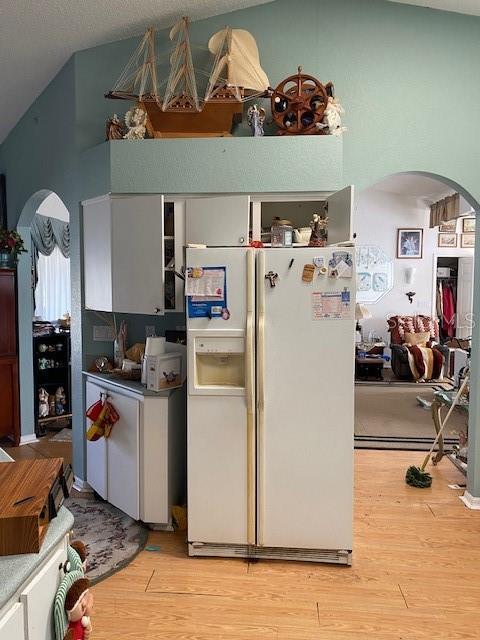 kitchen with arched walkways, white refrigerator with ice dispenser, light wood finished floors, and vaulted ceiling