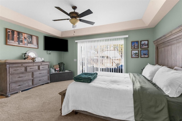 carpeted bedroom with ceiling fan, a tray ceiling, and access to exterior