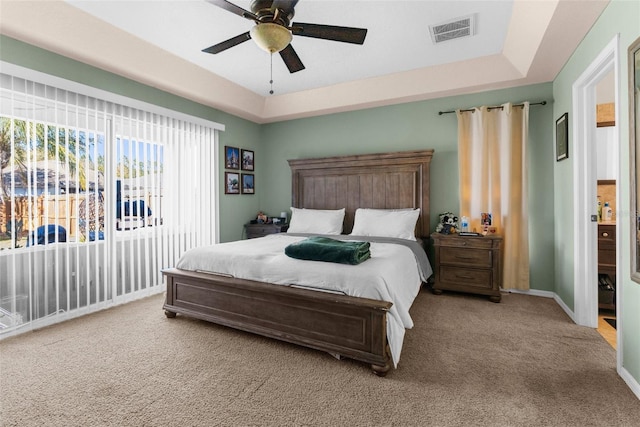 carpeted bedroom featuring visible vents, baseboards, a tray ceiling, a ceiling fan, and access to outside