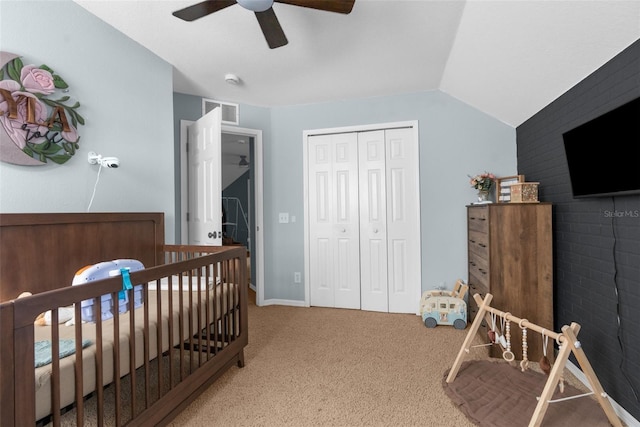 carpeted bedroom featuring visible vents, a crib, a closet, ceiling fan, and vaulted ceiling