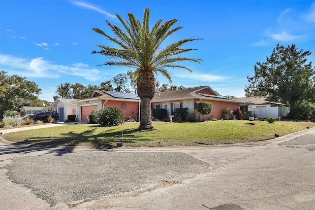 ranch-style house featuring solar panels, concrete driveway, an attached garage, fence, and a front lawn