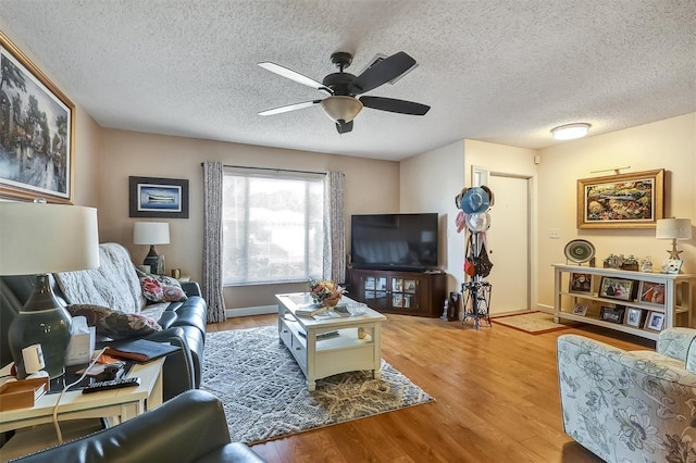 living room with ceiling fan, a textured ceiling, wood finished floors, and baseboards