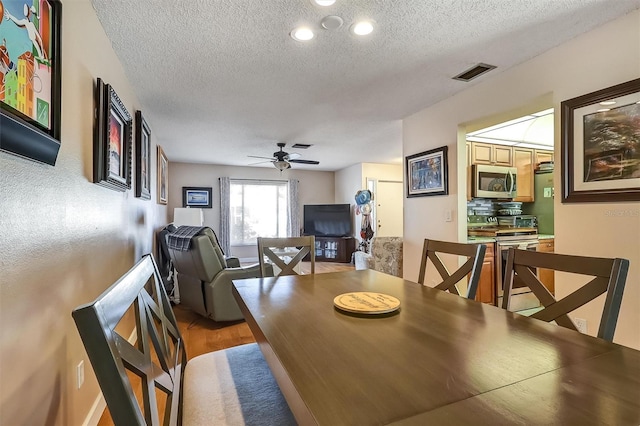 dining room with a textured ceiling, ceiling fan, light wood finished floors, and visible vents