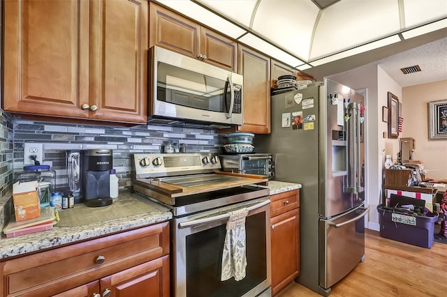 kitchen featuring light stone counters, appliances with stainless steel finishes, decorative backsplash, light wood finished floors, and brown cabinetry