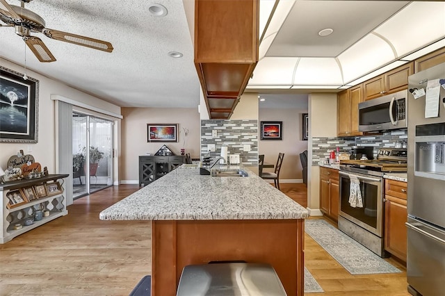 kitchen featuring brown cabinets, stainless steel appliances, light wood-style floors, a sink, and a peninsula