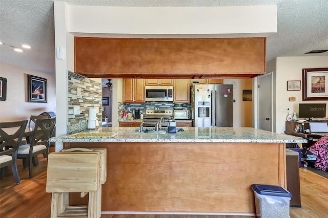 kitchen with light stone counters, a peninsula, appliances with stainless steel finishes, decorative backsplash, and light wood finished floors